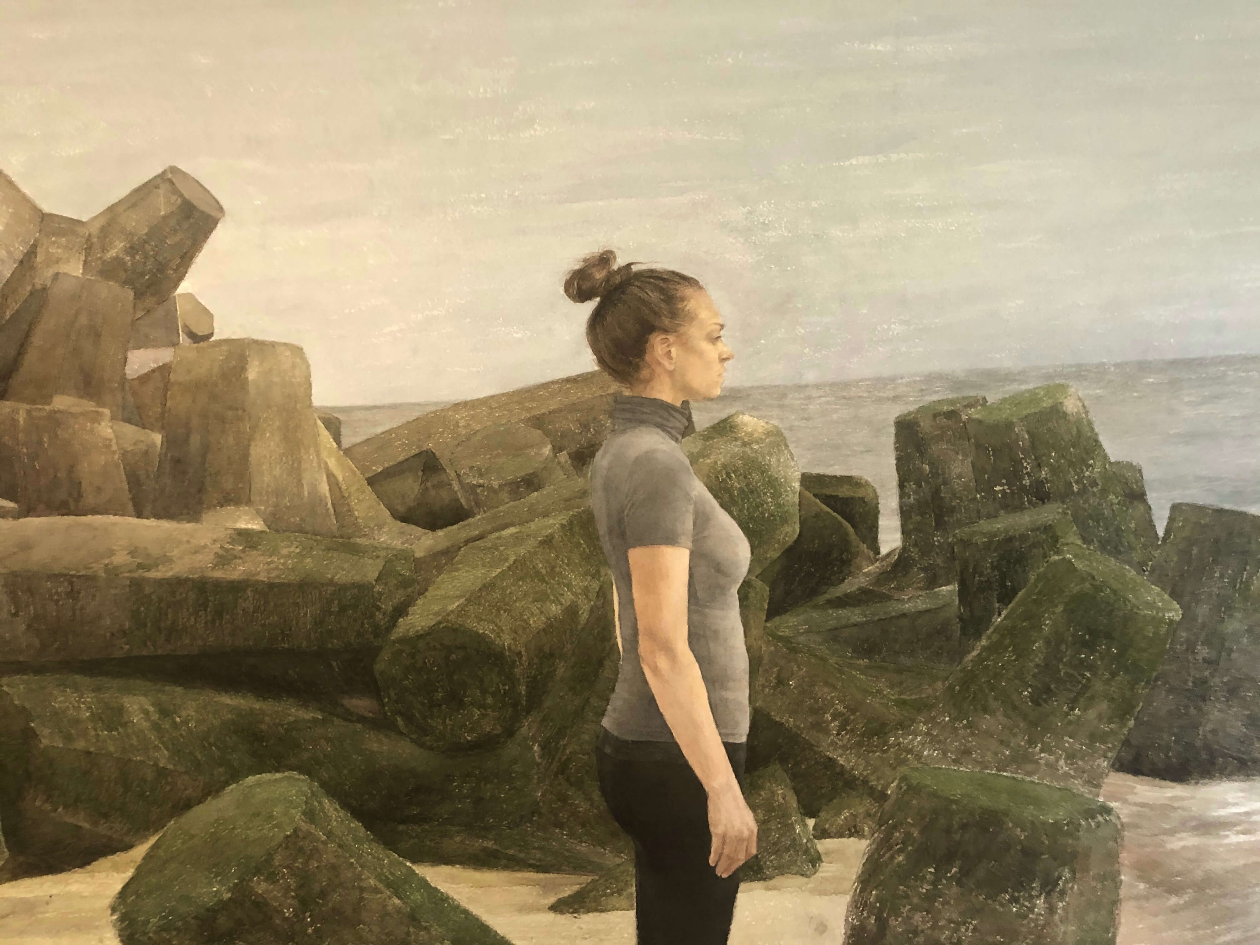Portrait of a woman in black leggings and grey top on beach by rocks by artist and painting holidays tutor Mario Andres Robinson.