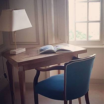 Desk with cream lamp and book. Blue chair and window.