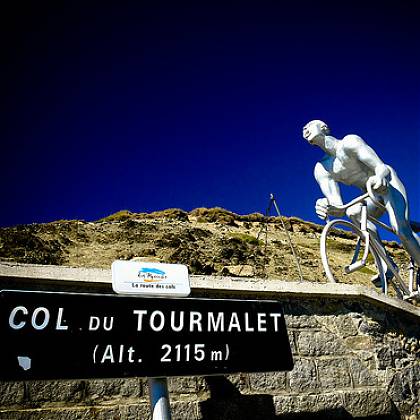 Col du Tourmalet road sign, statue man on bike, blue sky. 