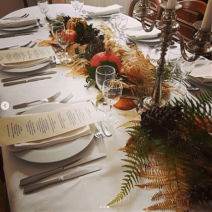 Table set for dinner, menus on white plates, pumpkins and foliage in center.