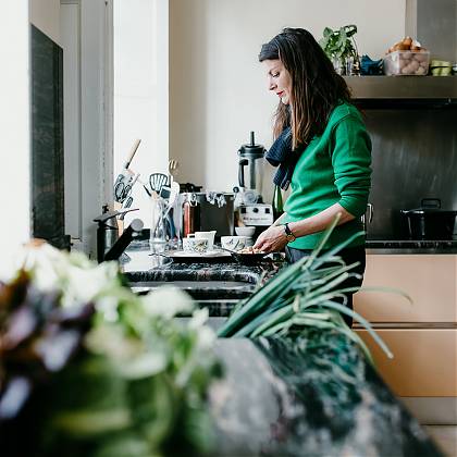 Woman in green cardigan standing by sink in kitchen.