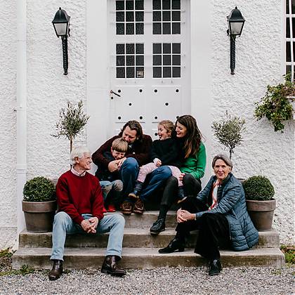 Four adults and two children sitting on steps of house in front of a white door.