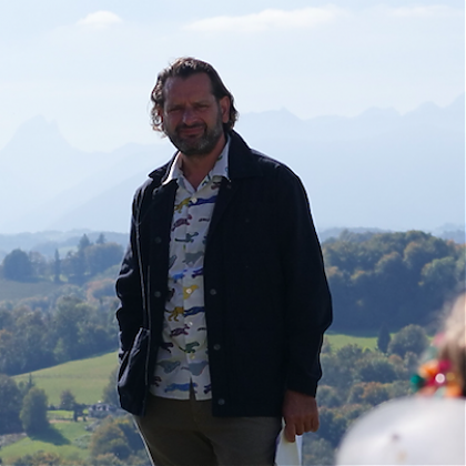 Portrait of male artist Xavier Micol wearing a shirt and jacket with fields in background.