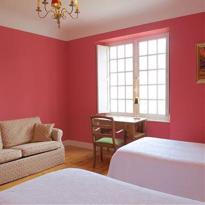 Bedroom with pink walls, beige sofa, dressing table and two single beds.