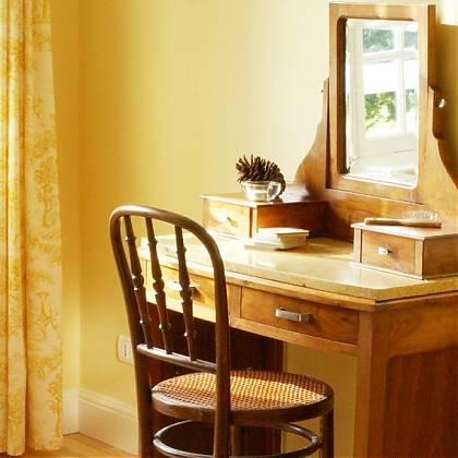 Dressing table with mirror and chair, yellow walls and curtain.
