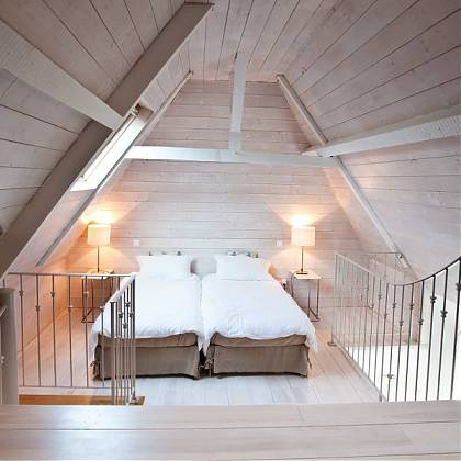 Bedroom with high ceiling in loft apartment. Two single beds with bedside tables and lamps.