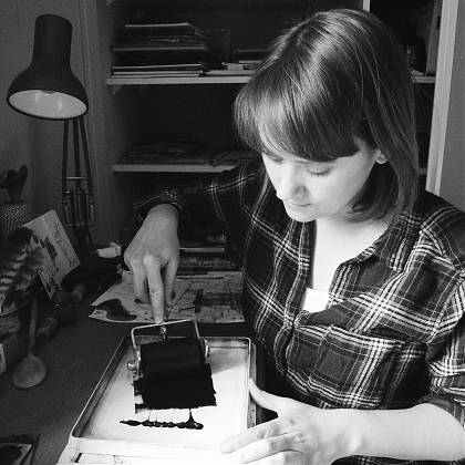 Black and white image of artist Emily Robertson rolling ink for lino-cutprinting.